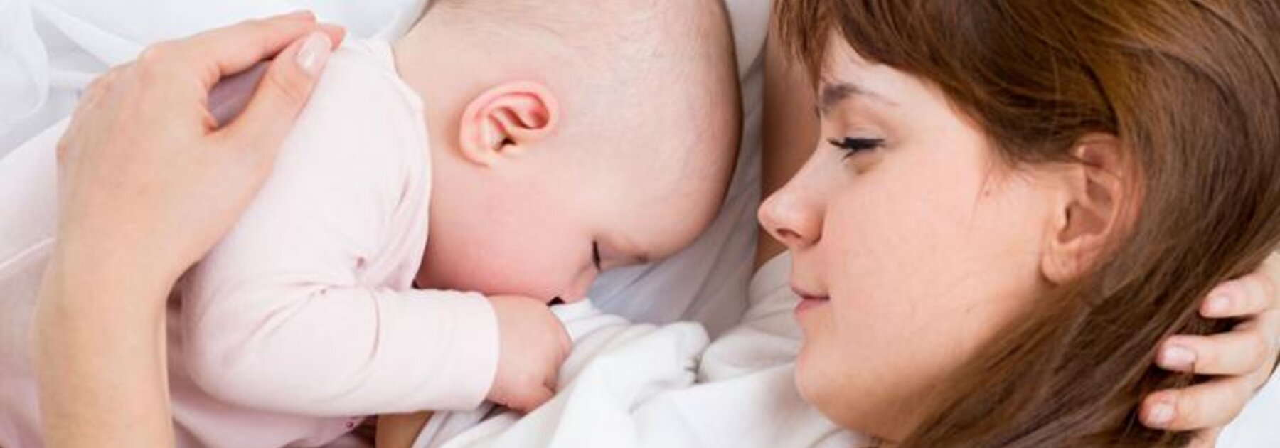 Breastfeeding Tips A mom watches as her baby sleeps in the bed next to her.