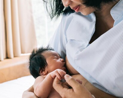 A baby holds its mother's finger while breastfeeding.
