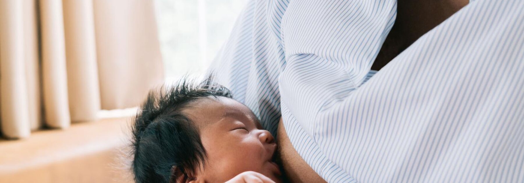 A baby holds its mother's finger while breastfeeding.
