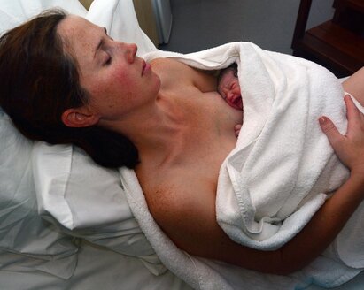A mother holding her baby wrapped in a towel immediately after birth.
