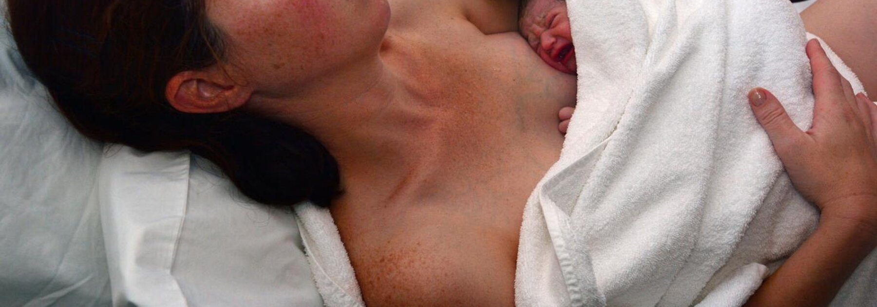 A mother holding her baby wrapped in a towel immediately after birth.