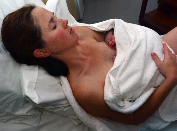 A mother holding her baby wrapped in a towel immediately after birth.