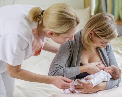 A mom breastfeeds her newborn baby while sitting at the end of the bed.