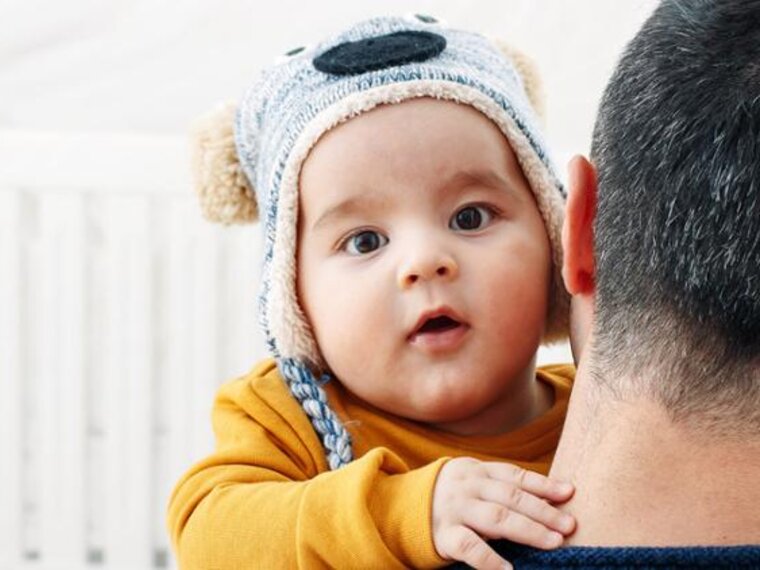 A father holding his baby in his arms as he looks into the camera, while outside.