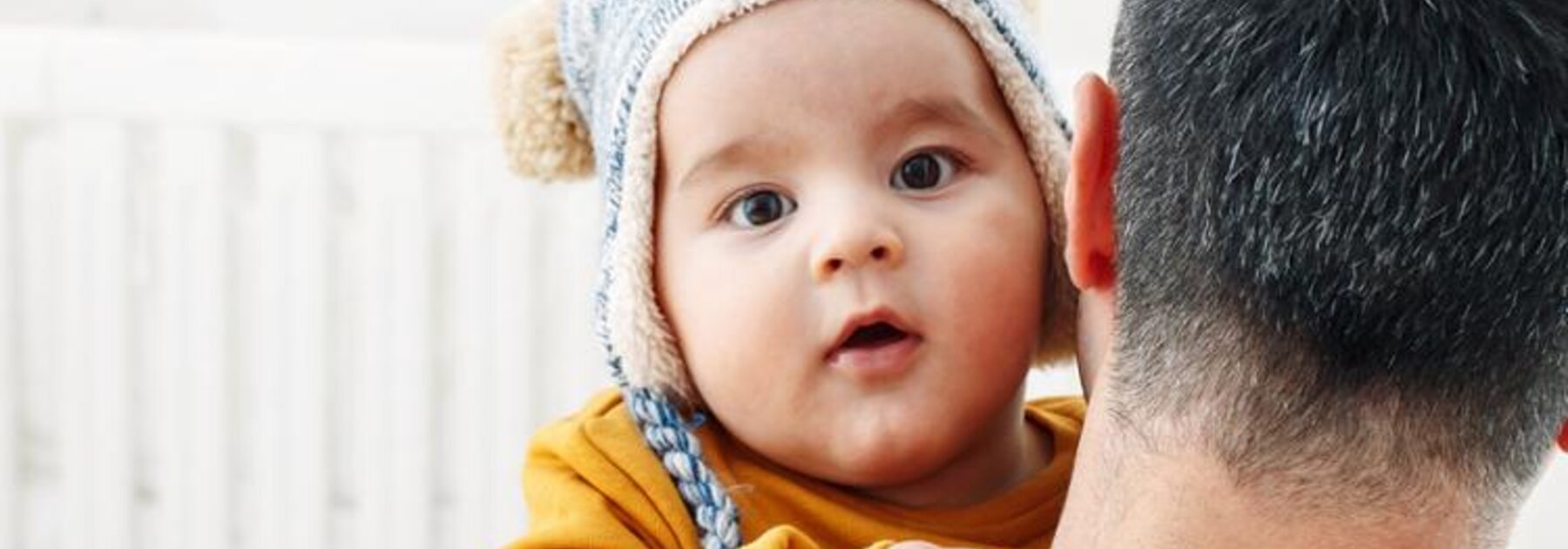 A father holding his baby in his arms as he looks into the camera, while outside.