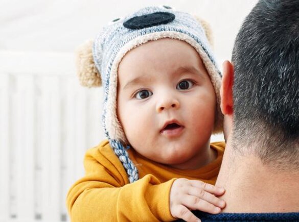 A father holding his baby in his arms as he looks into the camera, while outside.
