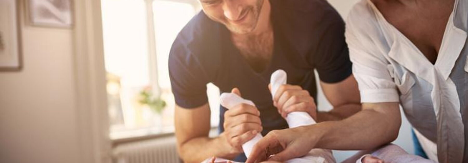 A father plays with his newborn baby while the mother looks on smiling.