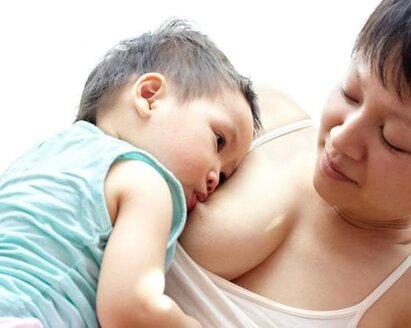 A mother is lying on her left side while her son is breastfeeding on her right side and resting quietly against her.