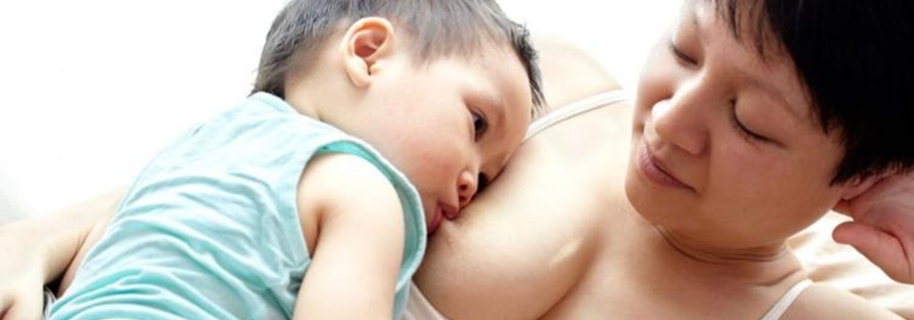 A mother is lying on her left side while her son is breastfeeding on her right side and resting quietly against her.