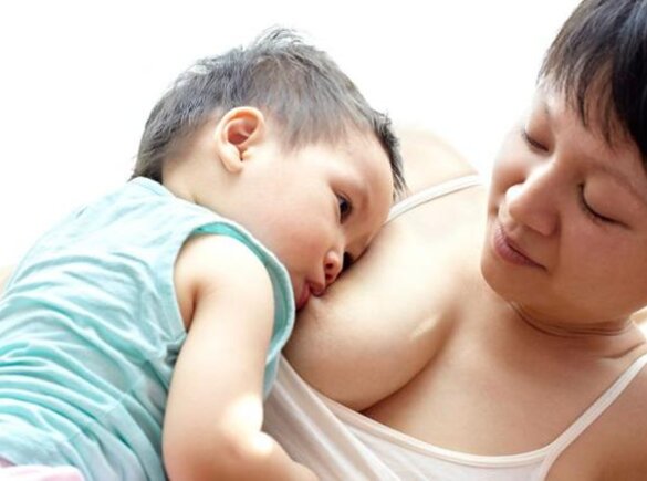 A mother is lying on her left side while her son is breastfeeding on her right side and resting quietly against her.