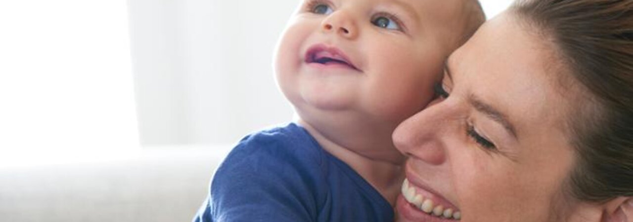 Une mère tient son bébé dans ses bras pendant qu'ils rient tous les deux.