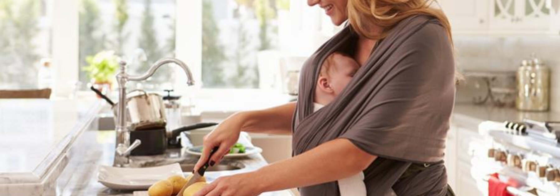 A mother prepares a healthy meal to support good nutrition during breastfeeding while her baby sleeps in a sling attached to her.