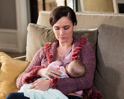 A mother breastfeeds her baby at home while sitting on the couch.