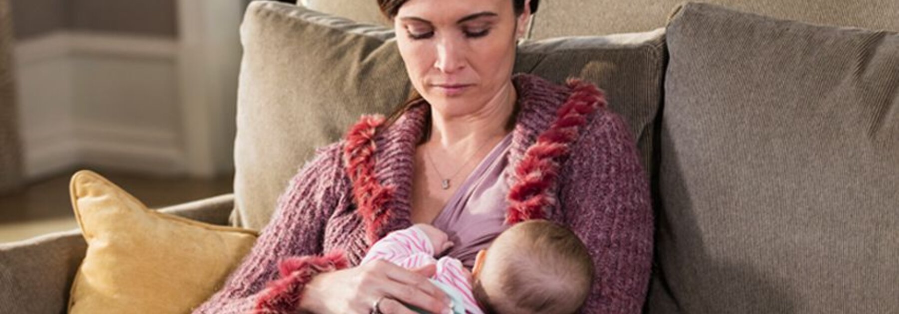 A mother breastfeeds her baby at home while sitting on the couch.