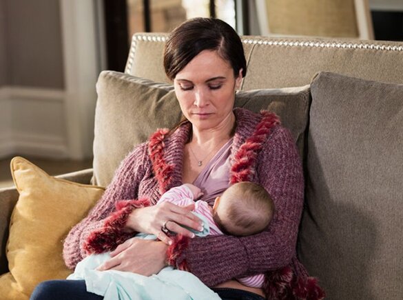 A mother breastfeeds her baby at home while sitting on the couch.