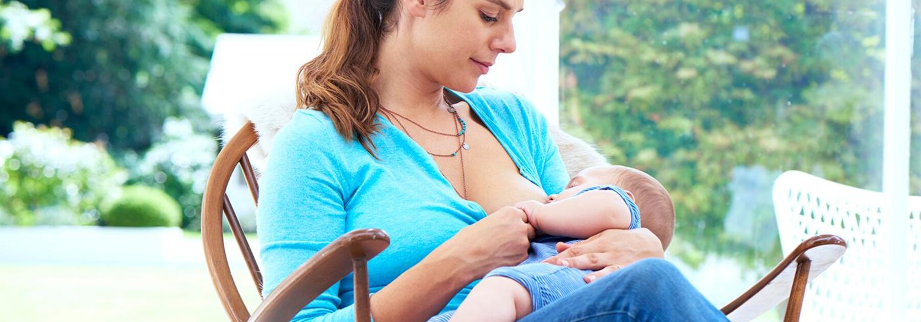 A mom breastfeeds her baby while sitting in a rocking chair by the window.