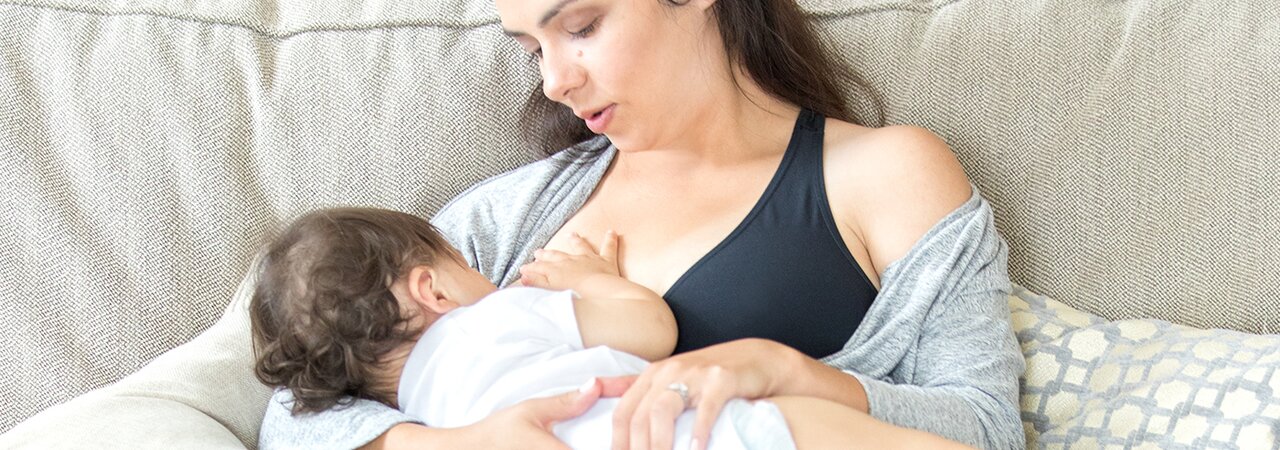 Een moeder die haar baby borstvoeding geeft terwijl ze een zwangerschapsbeha van Medela draagt.