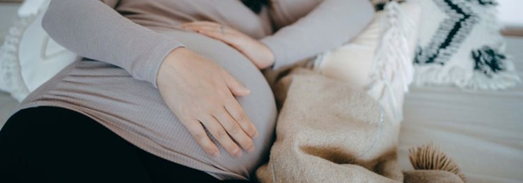 A pregnant woman lies asleep on her side in bed, holding her pregnant belly.