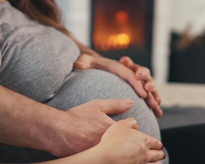 Woman sitting with her hands and her husbands hands on her pregnant belly.