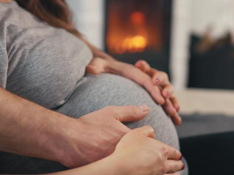 Woman sitting with her hands and her husbands hands on her pregnant belly.