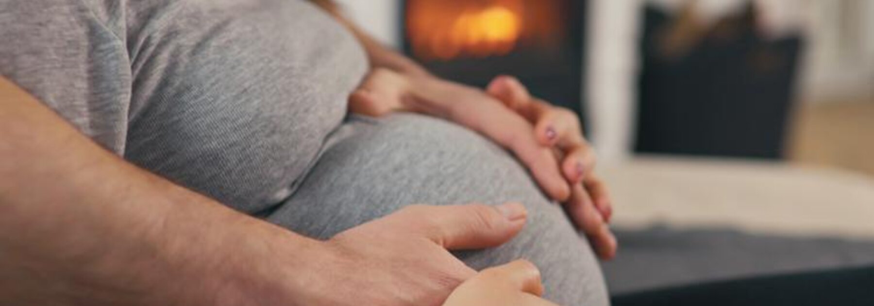 Woman sitting with her hands and her husbands hands on her pregnant belly.