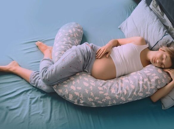 Van bovenaf gezien ligt een zwangere vrouw met een hoofdkussen in bed te slapen.