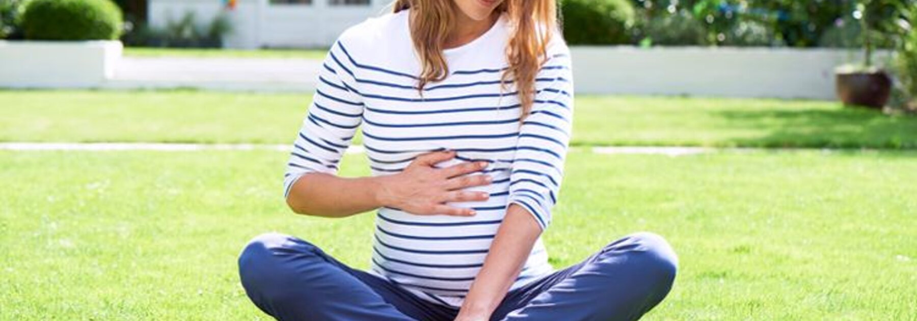 Une femme enceinte assise dans l'herbe, en train de lire un livre.