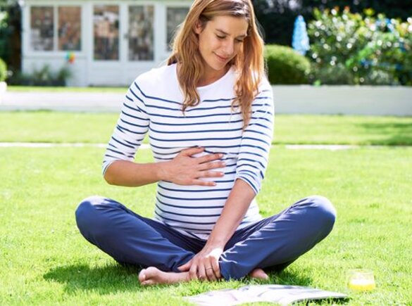 Une femme enceinte assise dans l'herbe, en train de lire un livre.