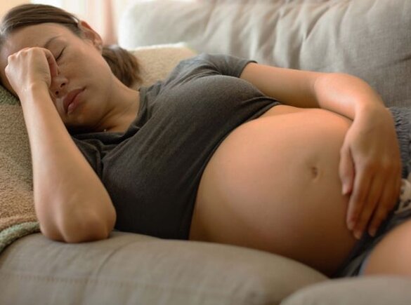 Femme enceinte tatouée, allongée sur un canapé, se tenant le ventre