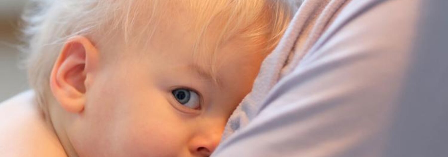 A child breastfeeds while sitting on his mother's lap.