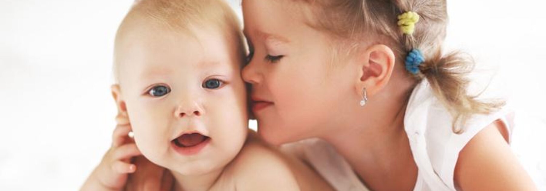 Eine Schwester gibt ihrem glücklichen kleinen Geschwisterchen einen Kuss auf die Wange, während sie auf dem Bauch in einem Bett liegen.