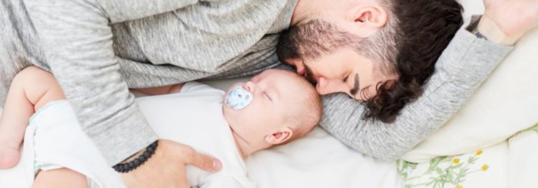 Vater und Baby schlafen im Bett nebeneinander, der Vater hält das Baby.