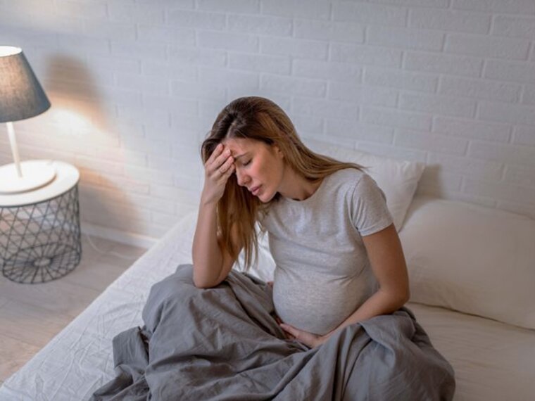 Maman enceinte assise dans son lit et souffrant d'un malaise.