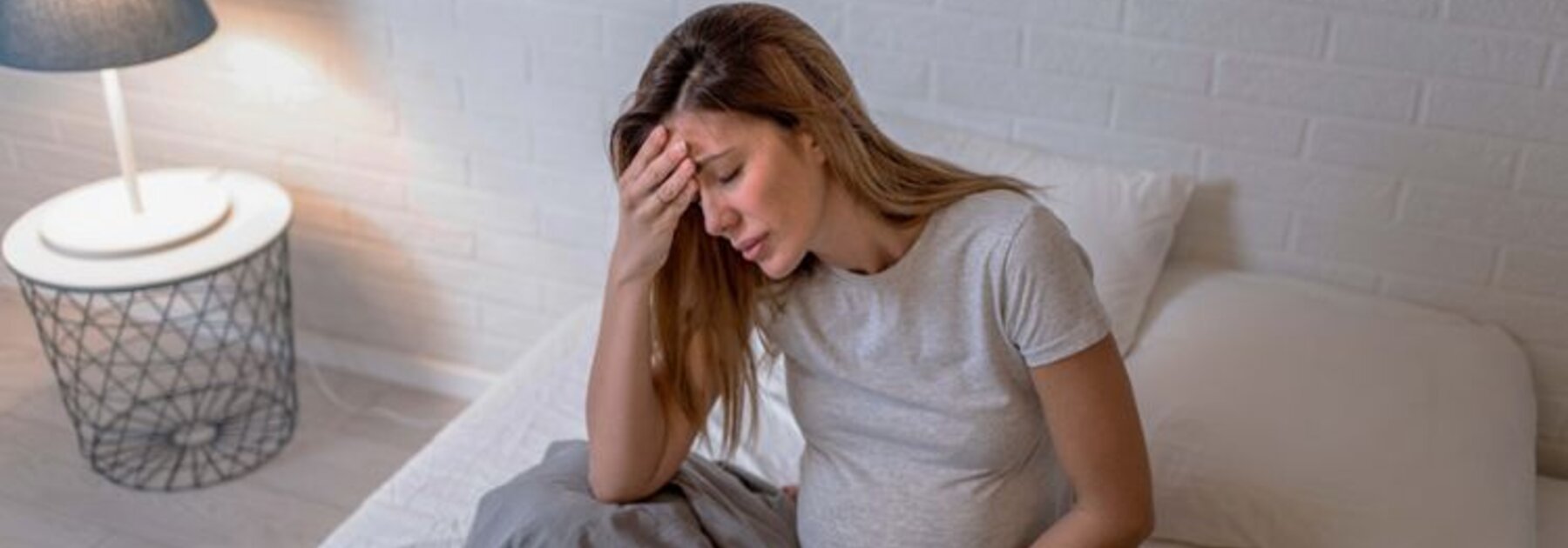 Maman enceinte assise dans son lit et souffrant d'un malaise.