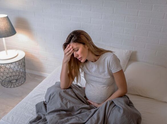 Maman enceinte assise dans son lit et souffrant d'un malaise.