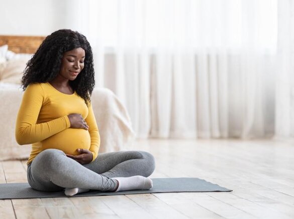 Maman enceinte assise sur un tapis de yoga.