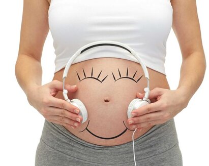 Eine Frau hält sich Kopfhörer an den schwangeren Bauch, um Musik zu hören.