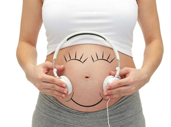 Eine Frau hält sich Kopfhörer an den schwangeren Bauch, um Musik zu hören.