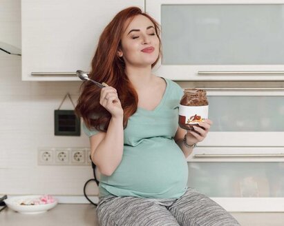 Eine schwangere Frau genießt es, Eis zu essen, während sie auf dem Küchentresen sitzt.
