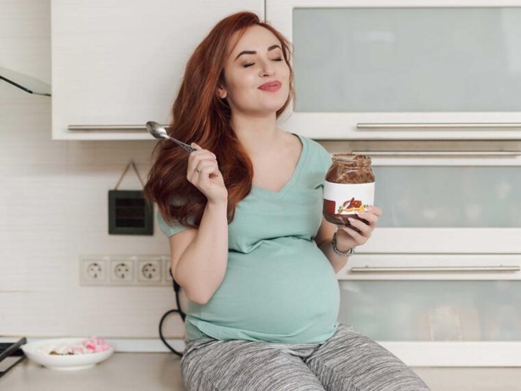 Eine schwangere Frau genießt es, Eis zu essen, während sie auf dem Küchentresen sitzt.