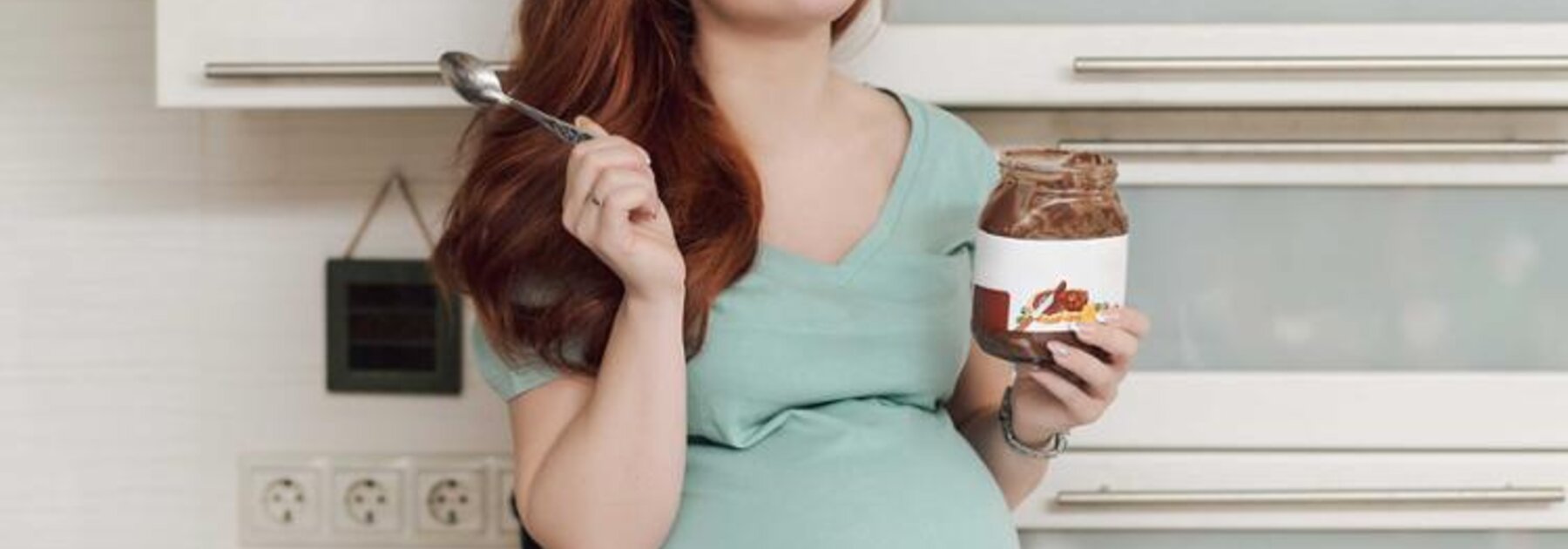 Eine schwangere Frau genießt es, Eis zu essen, während sie auf dem Küchentresen sitzt.