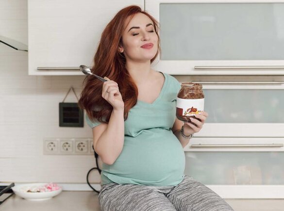 Eine schwangere Frau genießt es, Eis zu essen, während sie auf dem Küchentresen sitzt.