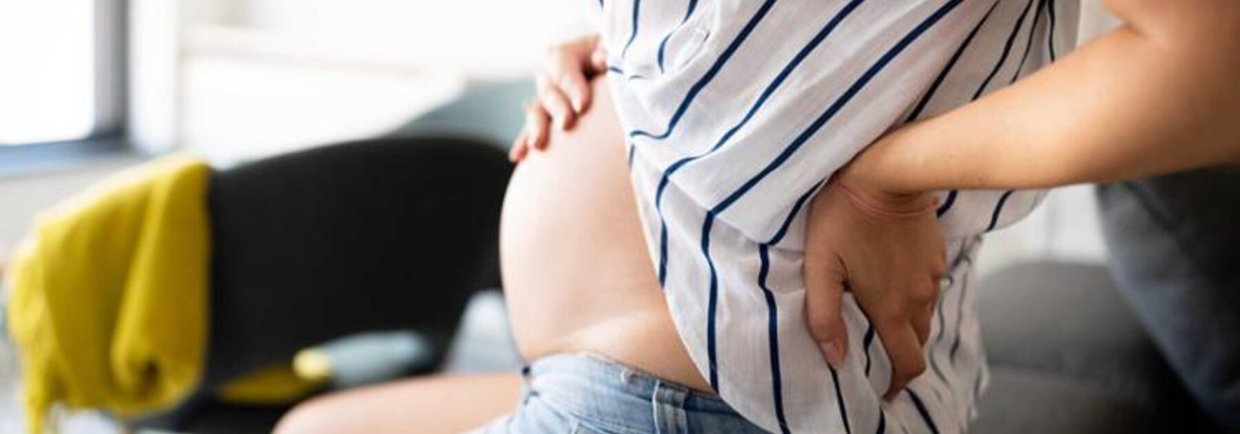 Eine schwangere Frau sitzt da und hält sich den Rücken und den schwangeren Bauch.