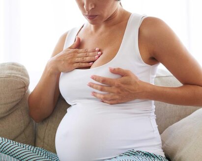 A pregnant woman massages her sore breast while sitting on a couch.