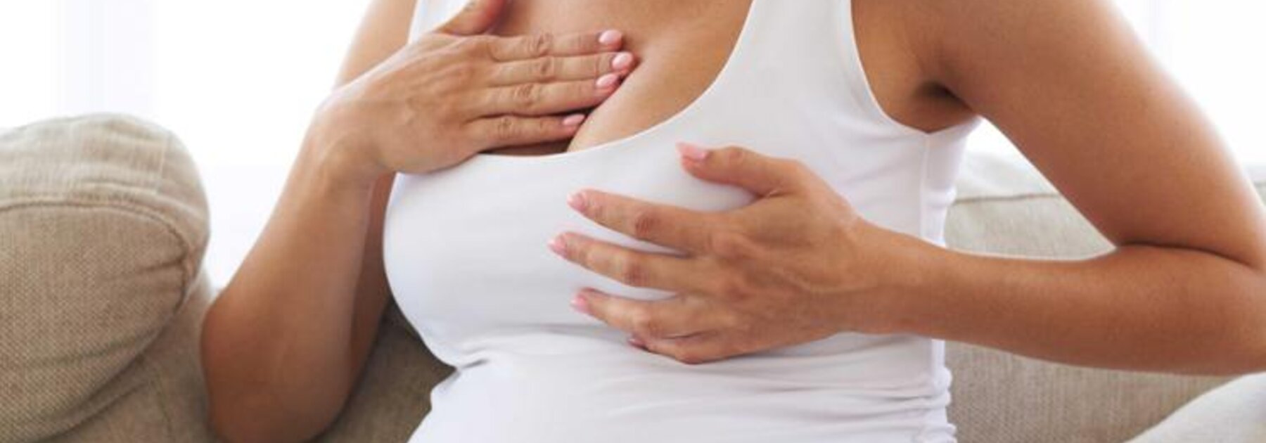 A pregnant woman massages her sore breast while sitting on a couch.