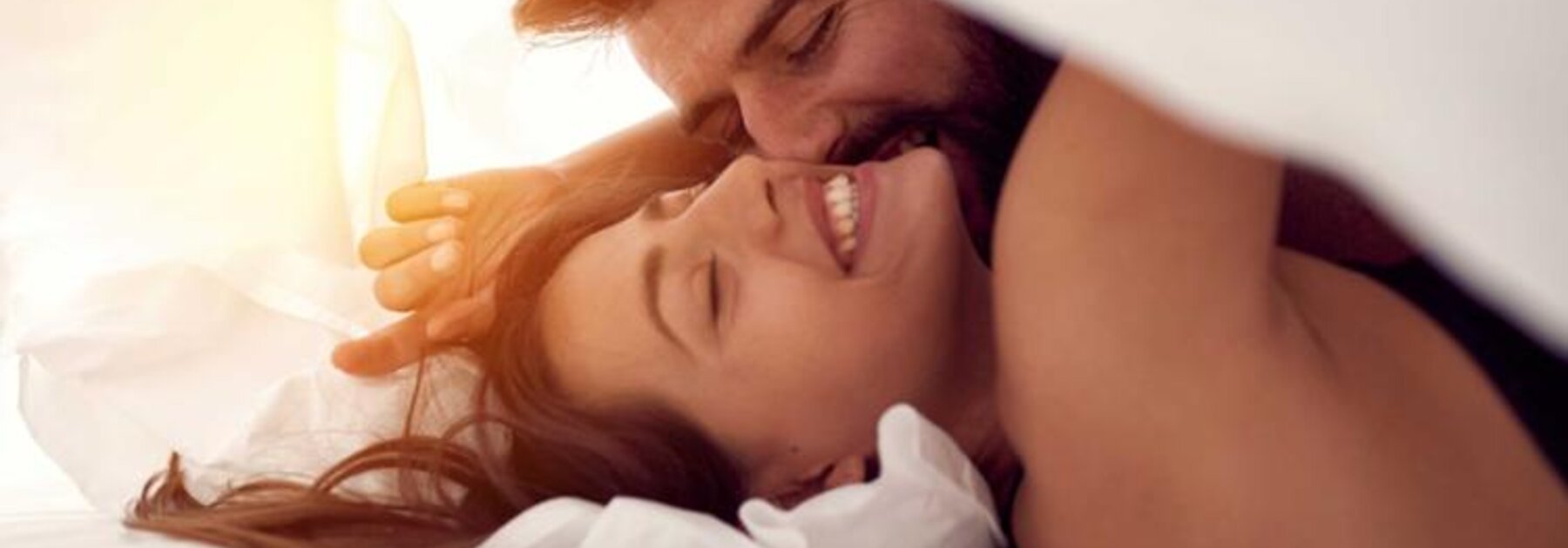 Ein Mann und eine Frau liegen zusammen im Bett und lachen.