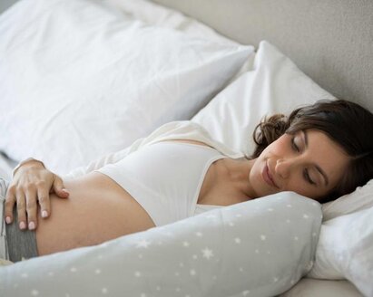 Frau liegt im Bett und hält ihren schwangeren Bauch
