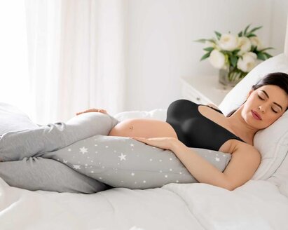 Eine schwangere Frau liegt schlafend im Bett mit einem Körperkissen.