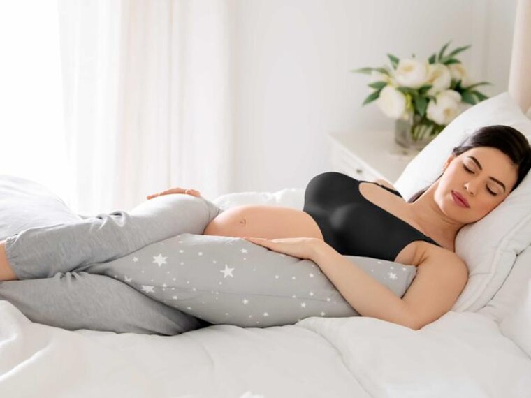 Eine schwangere Frau liegt schlafend im Bett mit einem Körperkissen.