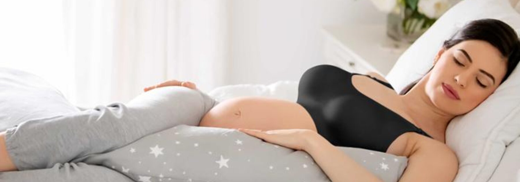 Eine schwangere Frau liegt schlafend im Bett mit einem Körperkissen.